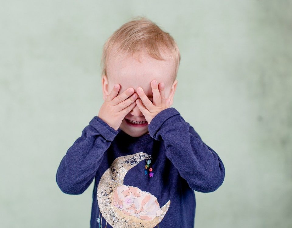child hiding face behind hands
